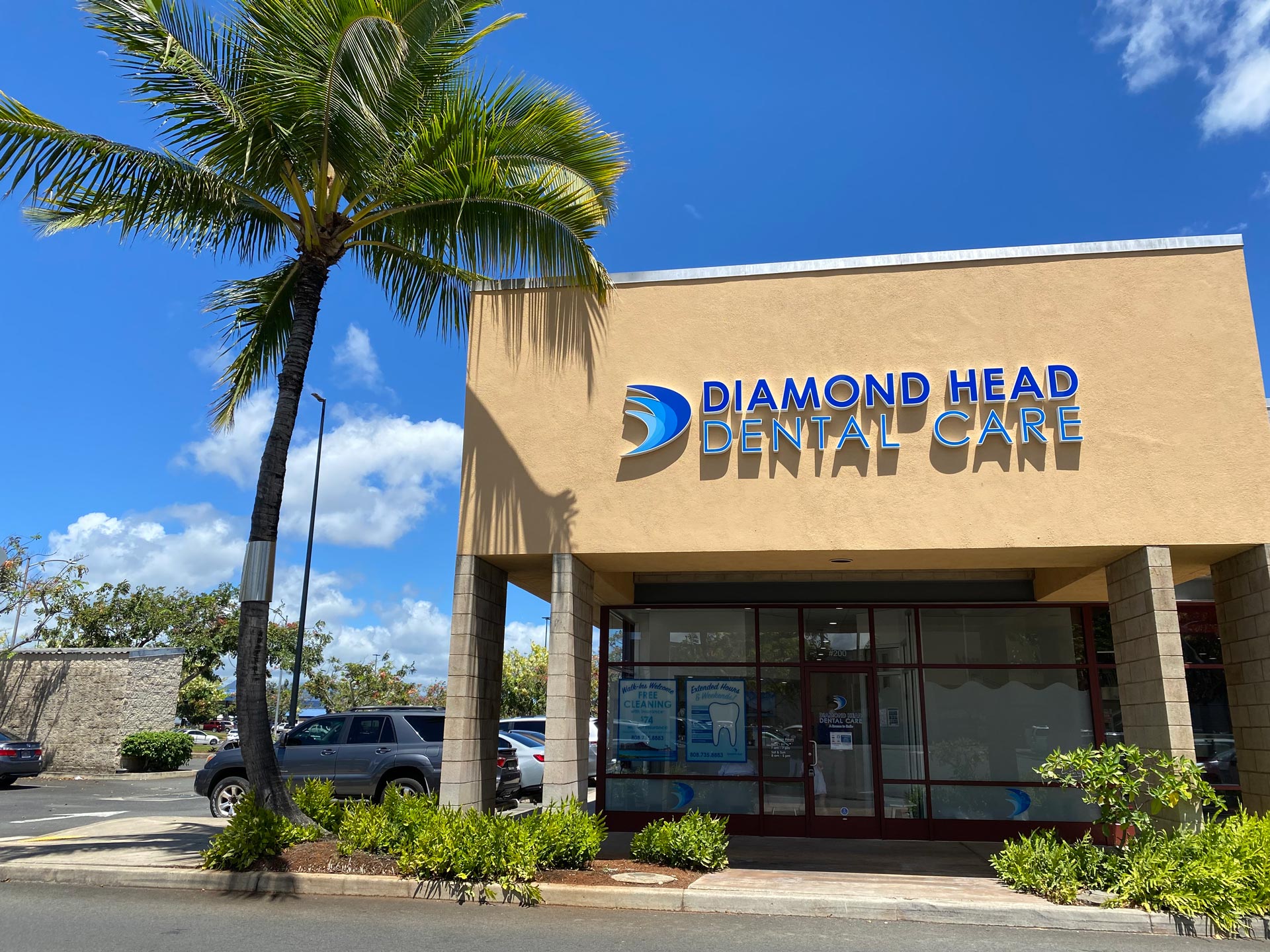 The image shows a building with a sign for  Diamond Head Dental Care  on a sunny day, featuring palm trees in front of the building and a clear blue sky above.