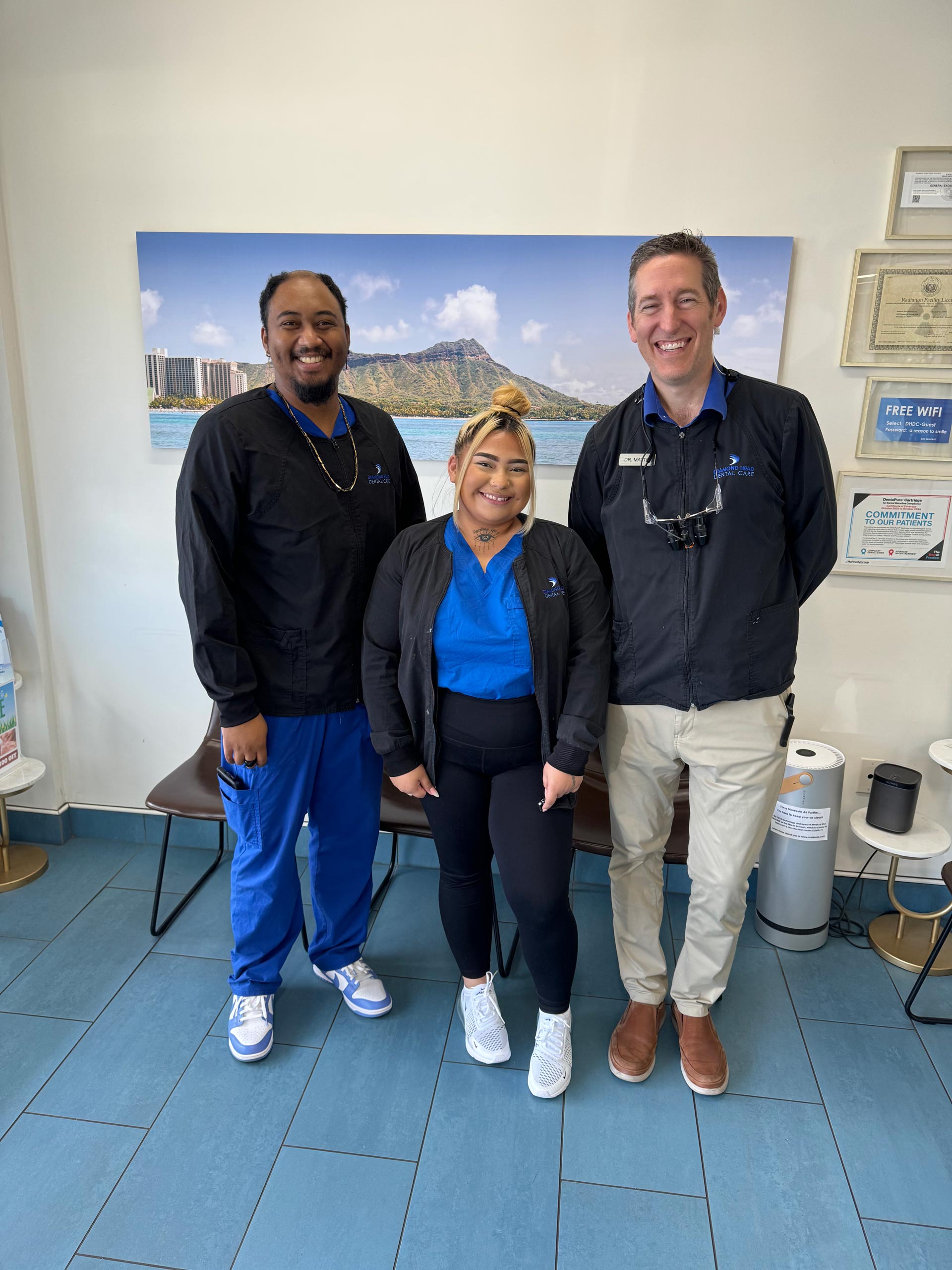 Three individuals posing in front of a sign with a scenic background, likely at a medical facility or clinic.