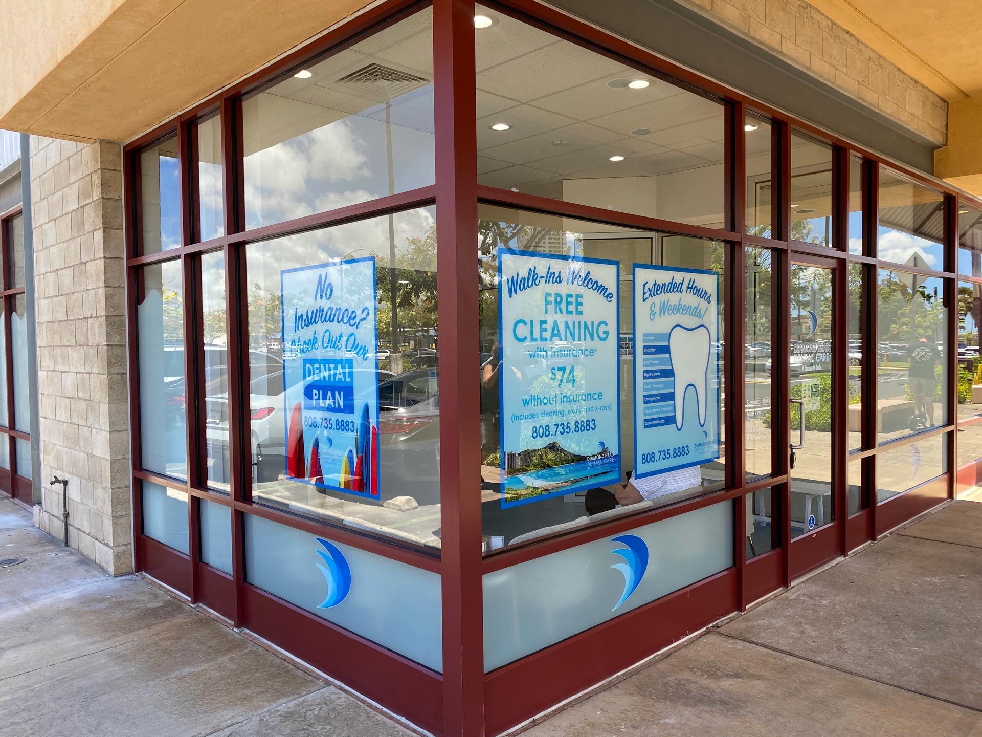 The image shows an exterior view of a storefront with a large window displaying cleaning supplies, featuring a sign advertising free masks and cleaning supplies inside, and a sign for a business named  Sandals  in the background.