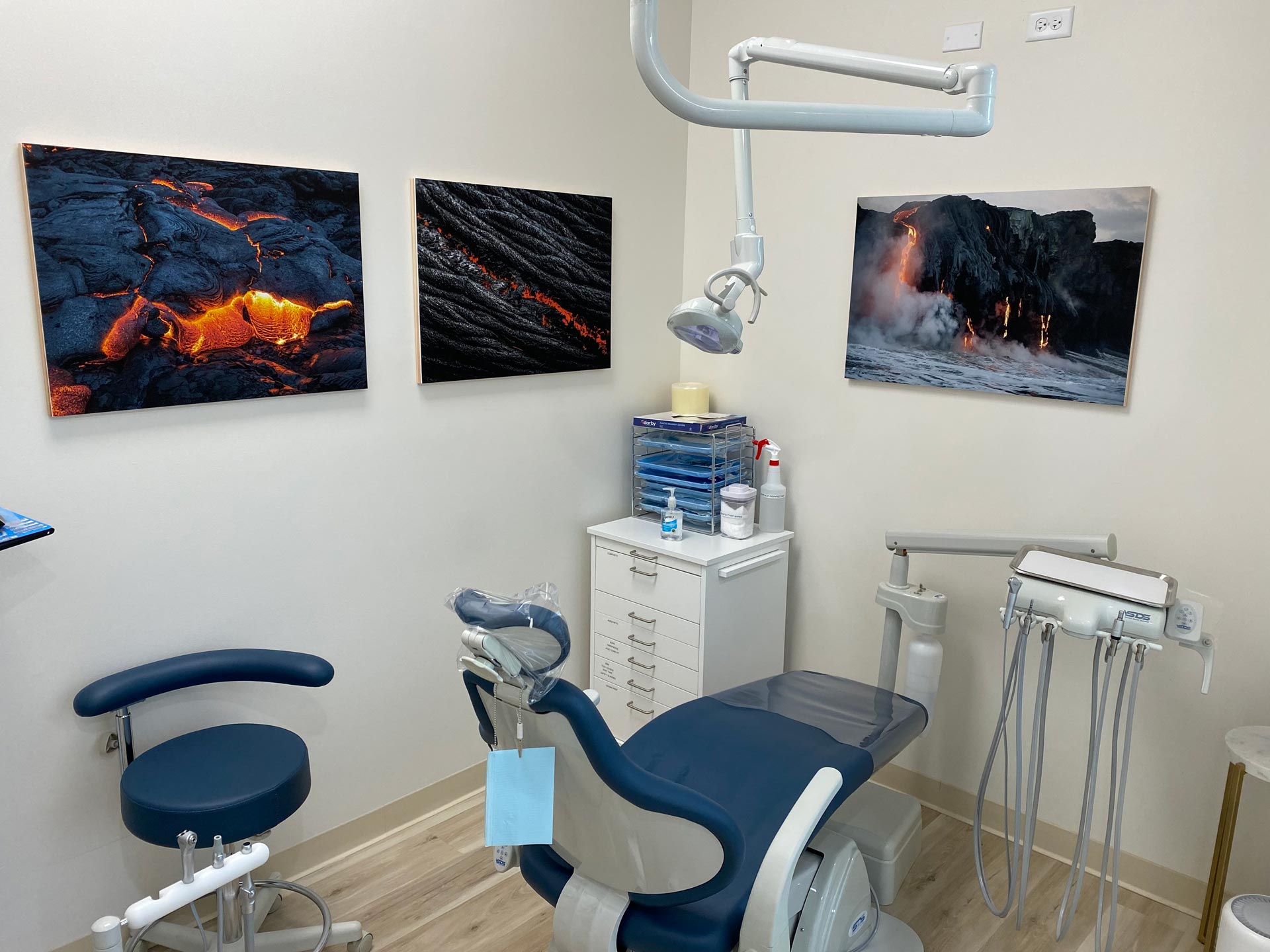 The image shows an interior view of a dental office with various pieces of equipment and a wall displaying artwork featuring volcanic landscapes.