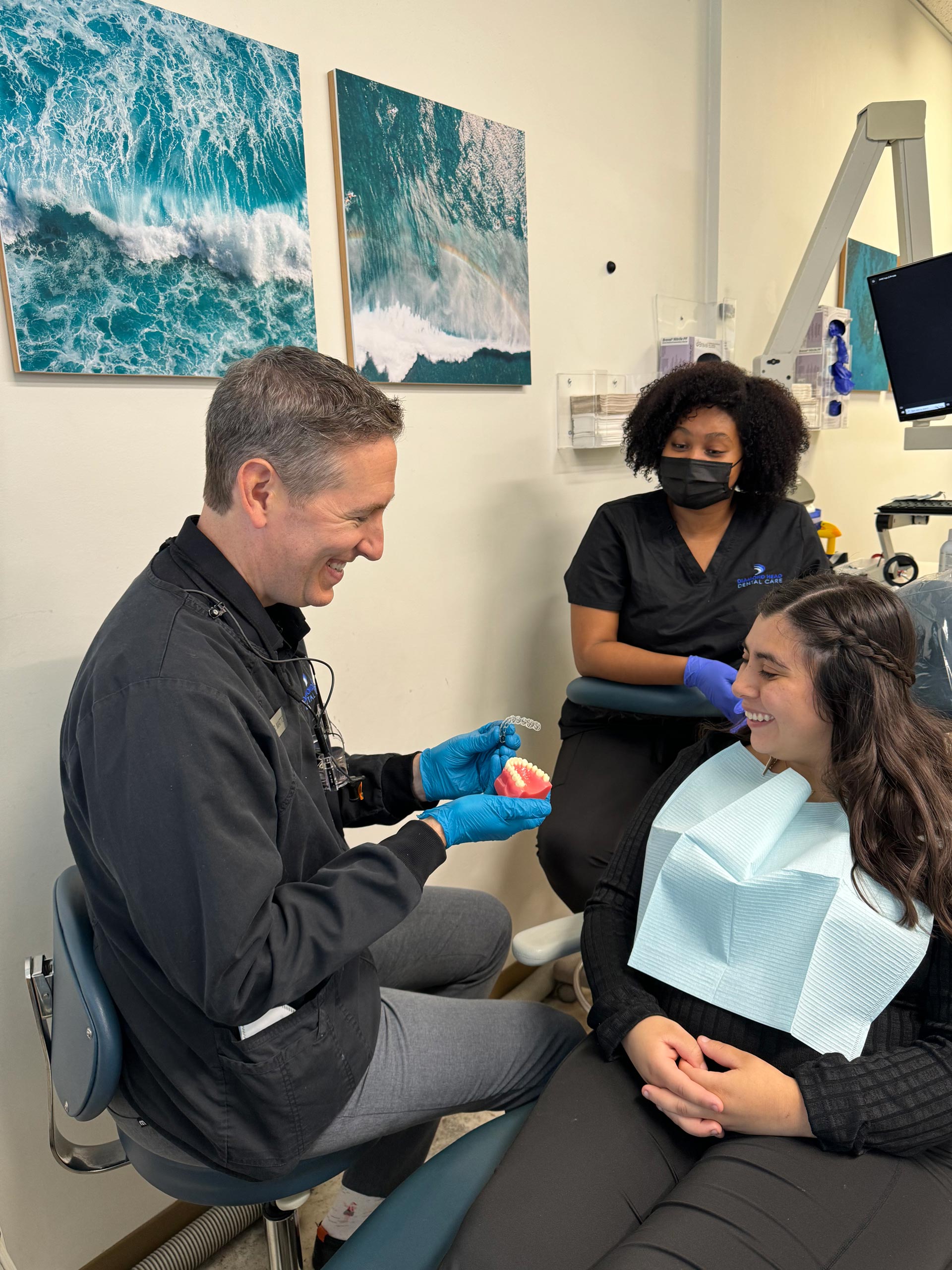A dentist examines a patient's teeth while seated on a chair with a blue background.