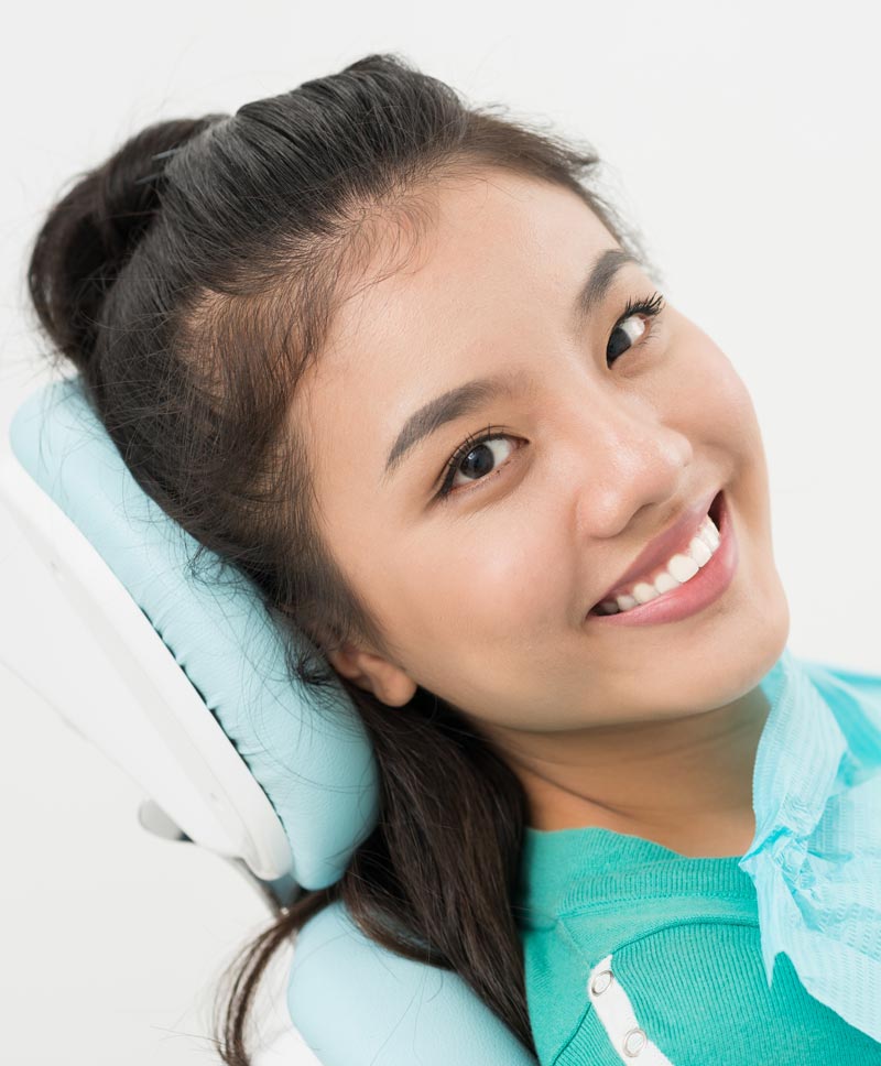 A young woman with light skin smiling at the camera while wearing headphones, likely for a hearing test or music session.