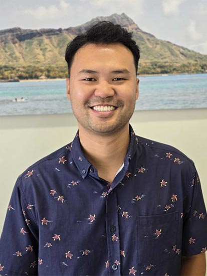 The image shows a man smiling at the camera with a mountainous landscape in the background.