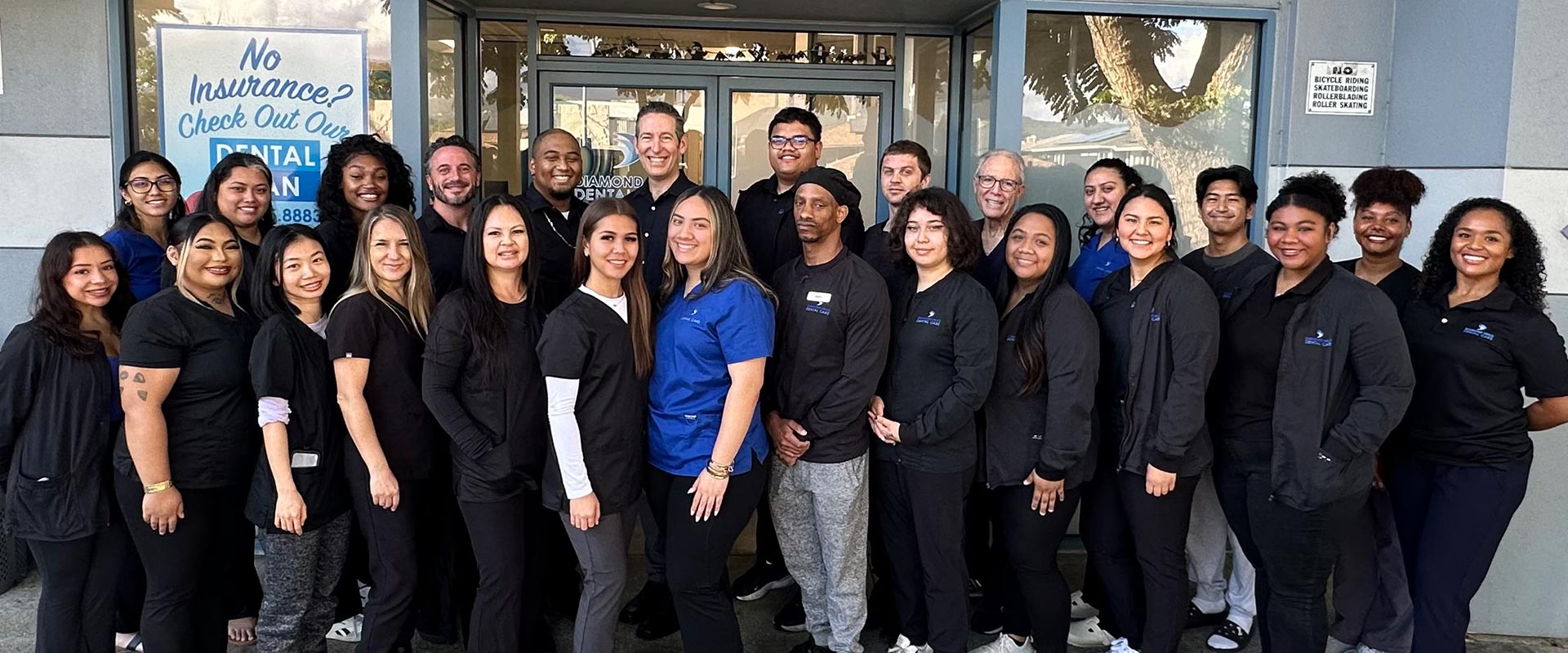 The image shows a group of people standing together outdoors, likely posing for a photograph, with a sign behind them that reads  No Entry,  indicating they are outside a restricted area.