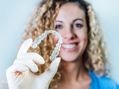 A woman holding a clear plastic container with a set of teeth-shaped objects inside.