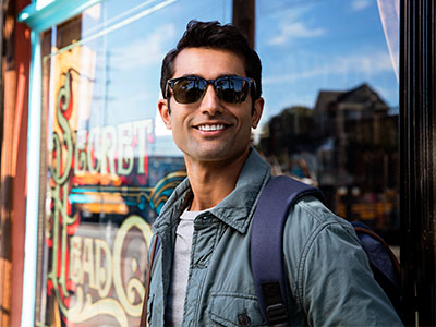 A man wearing sunglasses stands against a storefront window with signage.