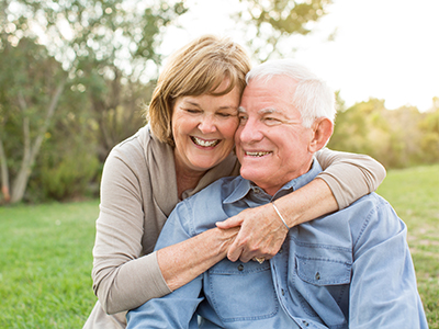 The image depicts an elderly couple sharing a warm embrace outdoors, with both individuals appearing content and happy.