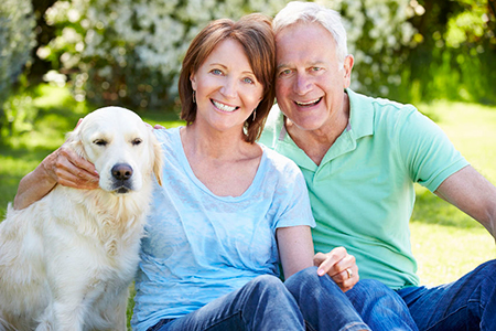 A man and woman sitting outdoors with a dog between them, smiling and posing for the photo.