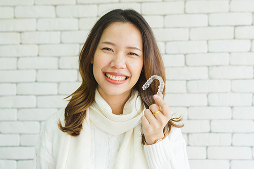 A woman holding a candy cane smiles at the camera against a brick wall background.