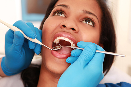 The image depicts a dental professional performing oral care on a patient, with the patient s mouth open wide and the dental professional using tools to clean or examine teeth.