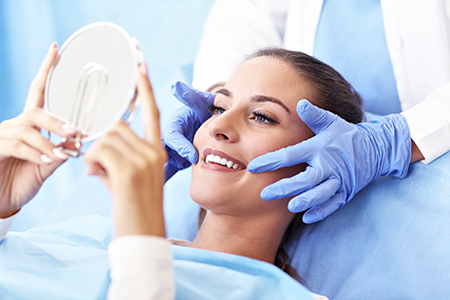 A woman receiving a facial treatment under the supervision of a professional, with a magnifying mirror and blue gloves visible.