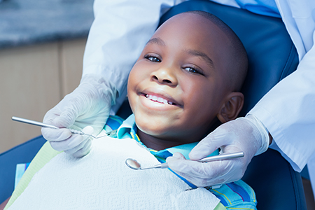 A young boy sitting in a dental chair receiving dental care from a dentist, with smiling faces on both.