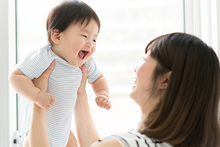 A woman holding a baby with a joyful expression while looking at him.