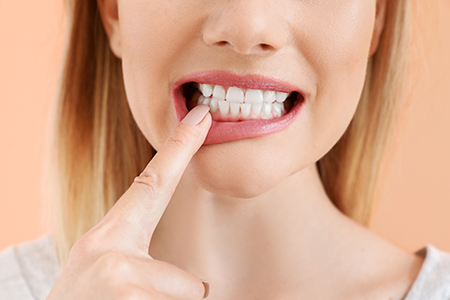A woman with a toothbrush in her mouth, pressing on her teeth while smiling.