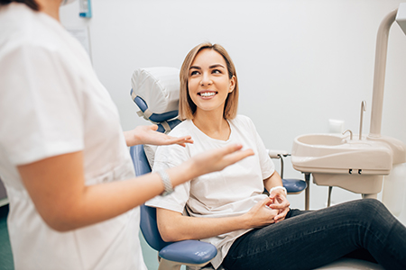 A woman sitting in a dental chair at a dentist s office with two dental professionals attending to her.