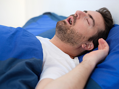 A man sleeping peacefully on a bed with pillows and a blue blanket.