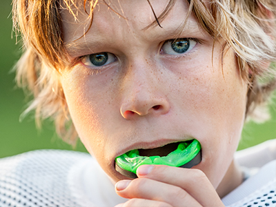 The image features two different photographs  the top photo shows a young boy with blonde hair wearing a football uniform, holding a green toothbrush in his mouth  the bottom photo presents the same boy, now with darker hair and still wearing a football uniform, but this time he is blowing bubbles.