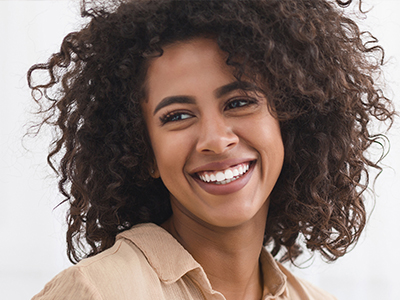 A woman with curly hair smiling at the camera, wearing a light-colored top, against a white background.